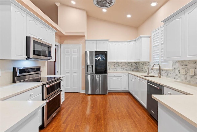 kitchen featuring light wood-type flooring, sink, white cabinets, vaulted ceiling, and appliances with stainless steel finishes