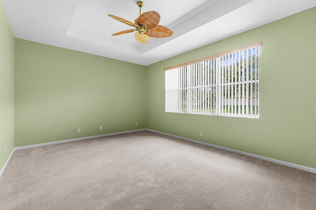 spare room with ceiling fan, a tray ceiling, and carpet flooring