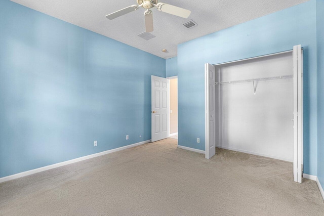 unfurnished bedroom featuring ceiling fan, light colored carpet, a textured ceiling, and a closet