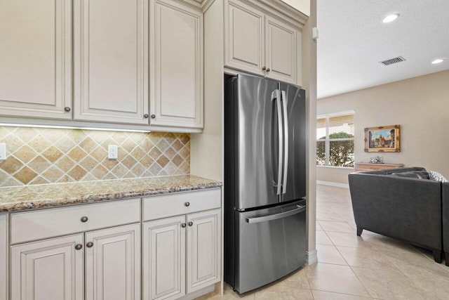 kitchen with a textured ceiling, stainless steel refrigerator, decorative backsplash, light tile patterned floors, and light stone countertops