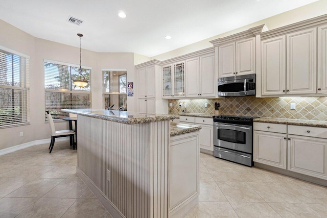 kitchen featuring light stone counters, appliances with stainless steel finishes, hanging light fixtures, and a kitchen island