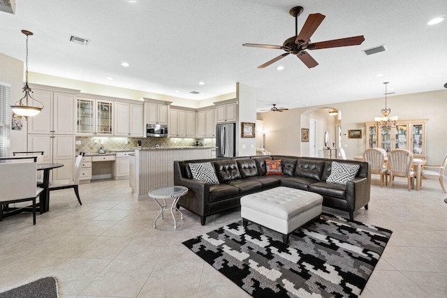 tiled living room with ceiling fan with notable chandelier