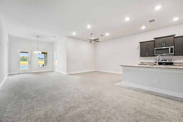 unfurnished living room with light carpet, sink, and ceiling fan with notable chandelier