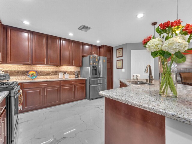 kitchen featuring tasteful backsplash, light stone counters, appliances with stainless steel finishes, decorative light fixtures, and sink