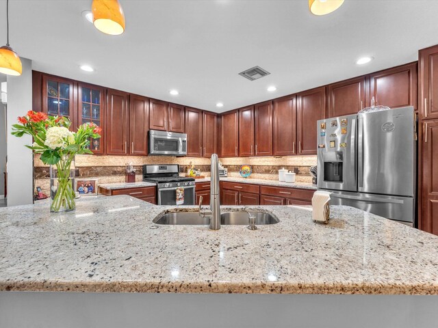 kitchen featuring light stone counters, appliances with stainless steel finishes, pendant lighting, decorative backsplash, and sink