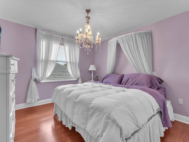 bedroom with wood-type flooring, a textured ceiling, and a notable chandelier