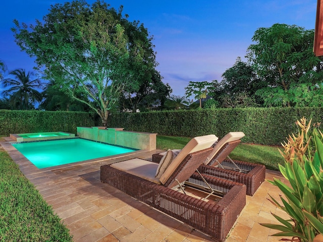 pool at dusk with a patio and an in ground hot tub