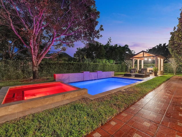 pool at dusk featuring a patio, an in ground hot tub, and a gazebo