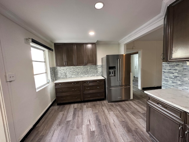 kitchen featuring ornamental molding, wood-type flooring, dark brown cabinets, backsplash, and stainless steel refrigerator with ice dispenser