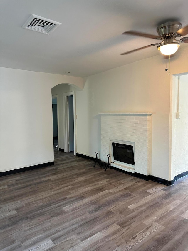 unfurnished living room featuring ceiling fan, a brick fireplace, and dark hardwood / wood-style flooring