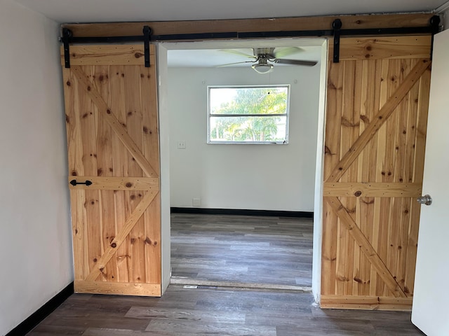 doorway with a barn door, dark wood-type flooring, and ceiling fan