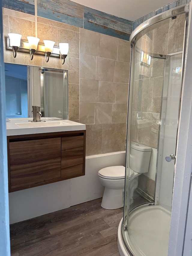 bathroom with tile walls, hardwood / wood-style floors, a shower with shower door, vanity, and toilet