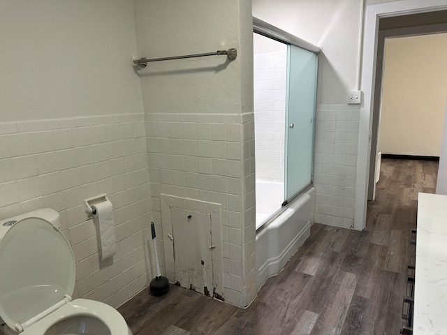 bathroom featuring tile walls, shower / bath combination with glass door, toilet, and wood-type flooring