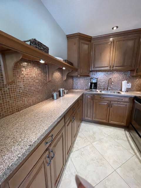 kitchen with light stone countertops, sink, backsplash, stainless steel electric range oven, and light tile patterned floors