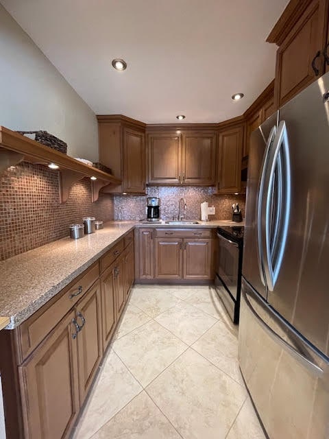 kitchen featuring decorative backsplash, stainless steel fridge, light tile patterned floors, black electric range, and sink