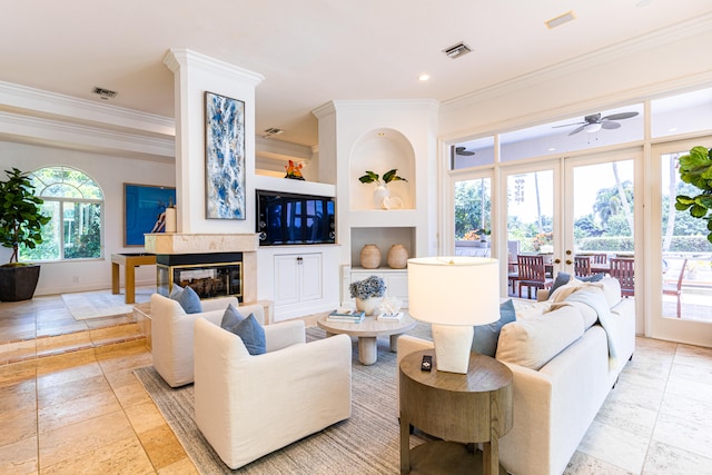 living room featuring built in shelves, a premium fireplace, ornamental molding, ceiling fan, and french doors