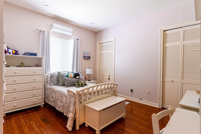 bedroom with two closets, dark hardwood / wood-style floors, and a wall mounted AC