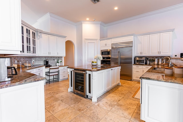 kitchen with wine cooler, built in appliances, decorative backsplash, crown molding, and dark stone countertops