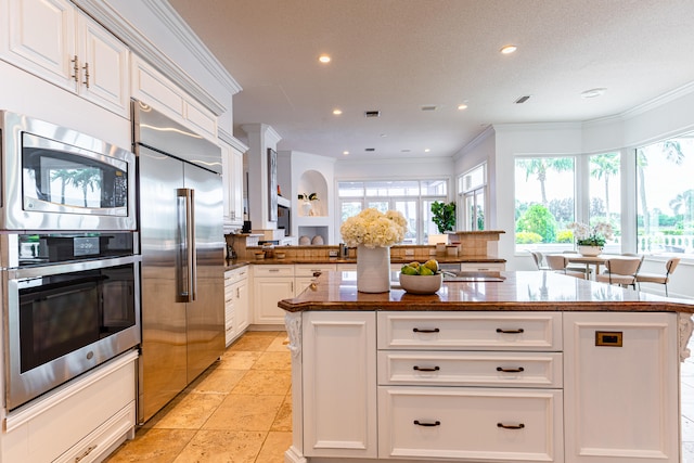 kitchen featuring built in appliances, ornamental molding, kitchen peninsula, and white cabinetry