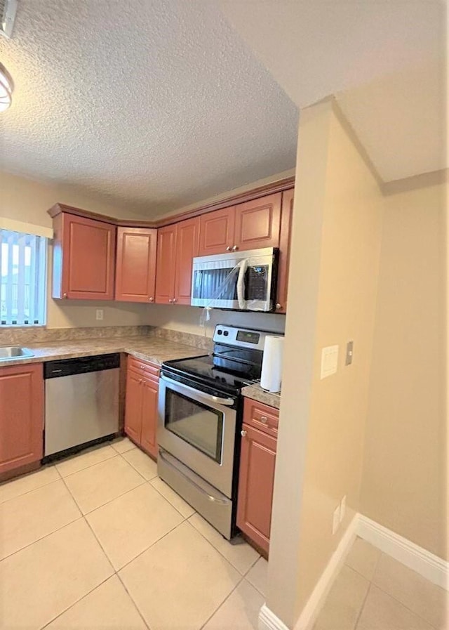 kitchen with a textured ceiling, appliances with stainless steel finishes, light tile patterned floors, and sink