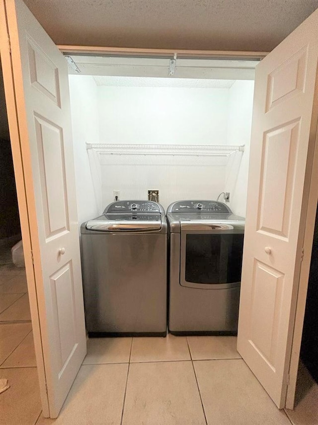 clothes washing area with a textured ceiling, light tile patterned floors, and washer and dryer