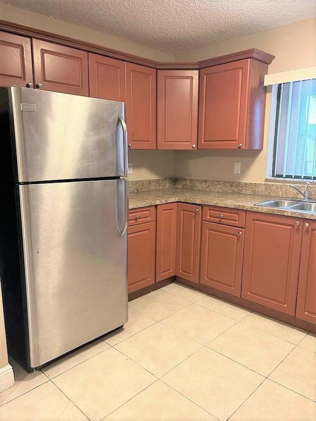 kitchen with a textured ceiling, sink, light tile patterned floors, and stainless steel fridge