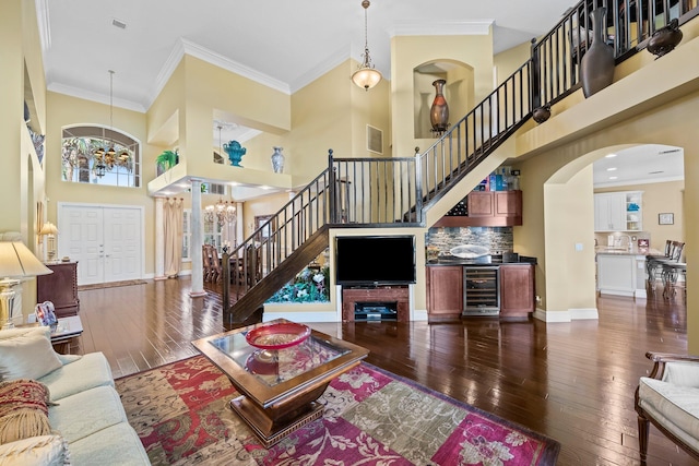 living room with beverage cooler, a towering ceiling, crown molding, dark hardwood / wood-style floors, and an inviting chandelier