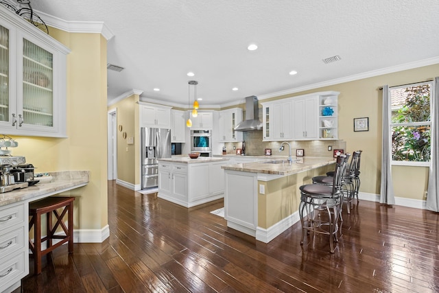 kitchen with appliances with stainless steel finishes, hanging light fixtures, kitchen peninsula, a breakfast bar, and wall chimney range hood