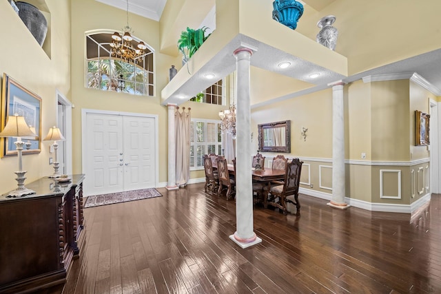 foyer entrance featuring dark hardwood / wood-style flooring, crown molding, a chandelier, and ornate columns