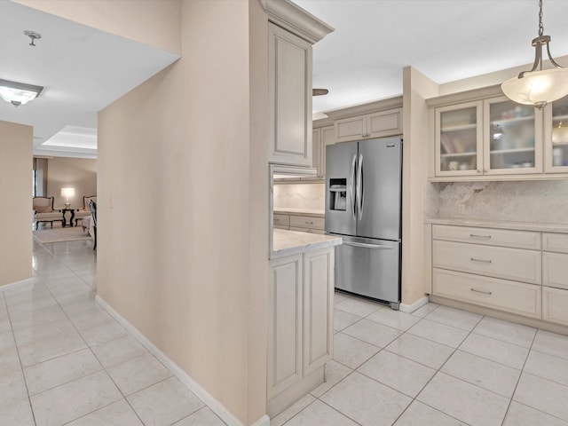 kitchen featuring light stone counters, stainless steel fridge, cream cabinets, decorative light fixtures, and light tile patterned flooring