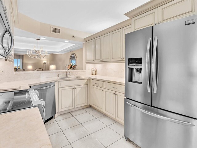 kitchen with stainless steel appliances, a raised ceiling, sink, a notable chandelier, and cream cabinetry