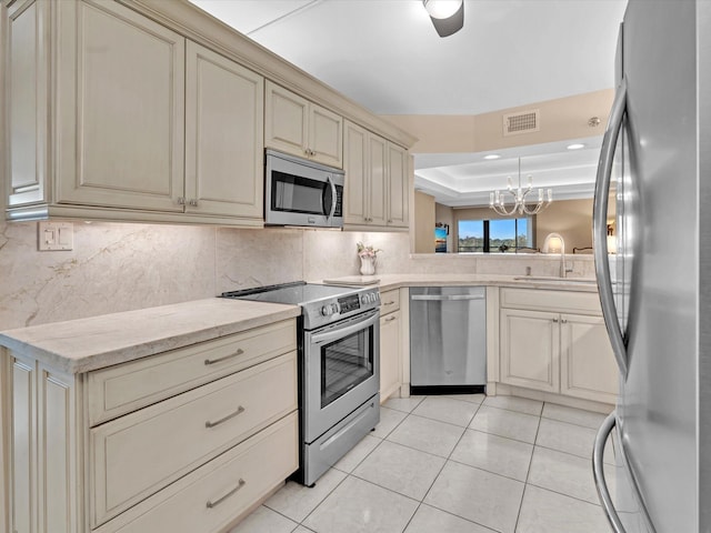 kitchen featuring stainless steel appliances, sink, cream cabinetry, hanging light fixtures, and light tile patterned flooring