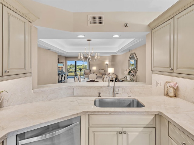 kitchen featuring sink, a raised ceiling, a notable chandelier, pendant lighting, and cream cabinetry