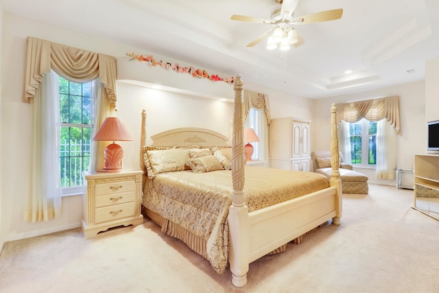 bedroom featuring carpet flooring, a tray ceiling, multiple windows, and ceiling fan