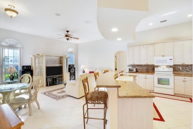 kitchen featuring ceiling fan, sink, white appliances, a breakfast bar, and light stone countertops