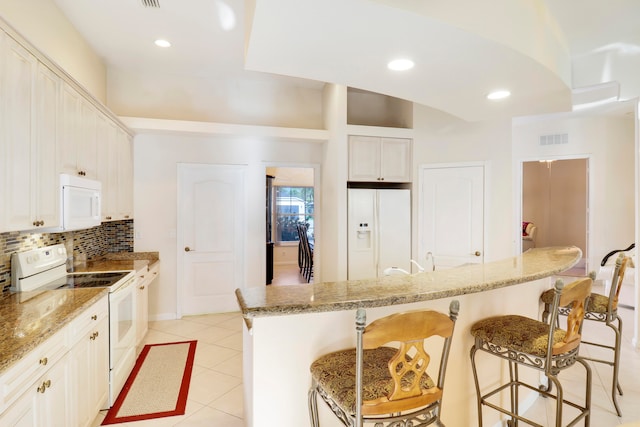 kitchen with a breakfast bar area, white cabinetry, a kitchen island, white appliances, and light stone countertops