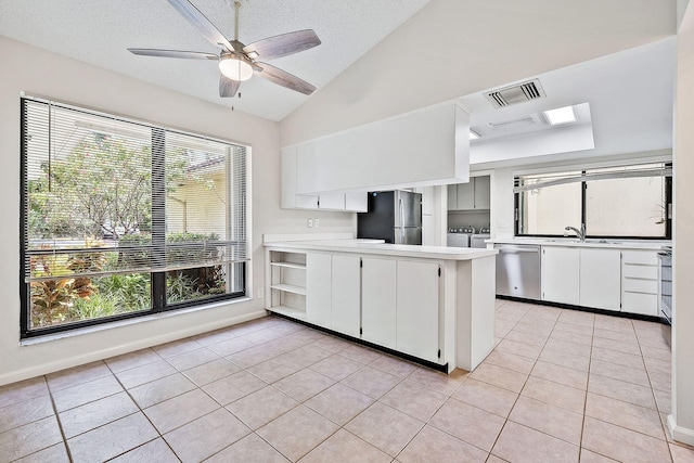 kitchen with lofted ceiling with skylight, ceiling fan, stainless steel appliances, and white cabinets