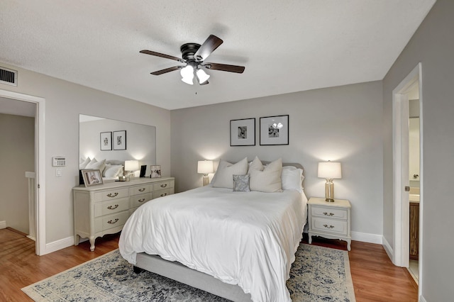 bedroom featuring ceiling fan, a textured ceiling, light hardwood / wood-style flooring, and connected bathroom