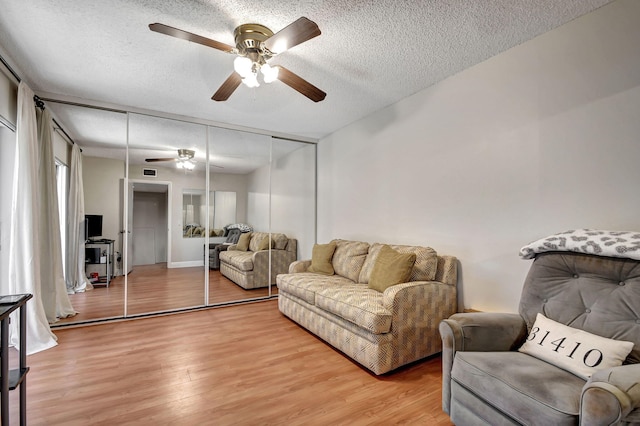 living room featuring wood-type flooring, ceiling fan, and a textured ceiling