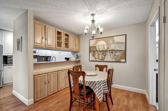 dining area featuring light wood-type flooring, a textured ceiling, sink, and a notable chandelier