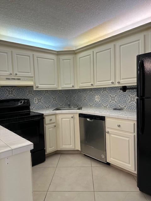 kitchen featuring light tile patterned flooring, backsplash, cream cabinetry, black appliances, and tile countertops