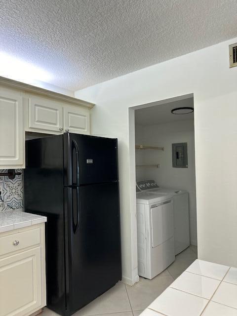 kitchen with black fridge, electric panel, light tile patterned floors, a textured ceiling, and independent washer and dryer