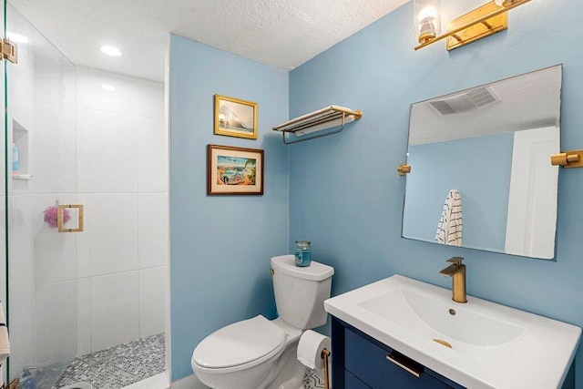 bathroom featuring a tile shower, vanity, toilet, and a textured ceiling