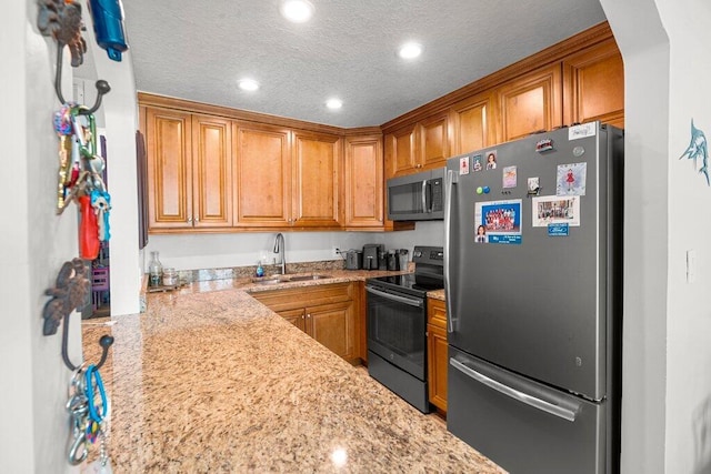 kitchen featuring light stone countertops, a textured ceiling, appliances with stainless steel finishes, and sink