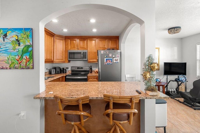 kitchen featuring a textured ceiling, appliances with stainless steel finishes, kitchen peninsula, and a kitchen breakfast bar