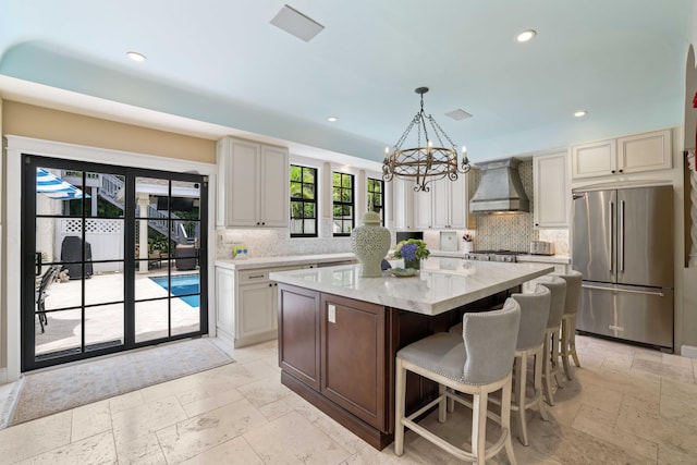 kitchen featuring pendant lighting, high quality fridge, wall chimney exhaust hood, a center island, and a notable chandelier