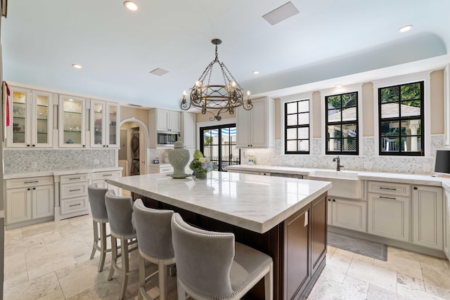 kitchen featuring a center island, tasteful backsplash, stainless steel microwave, an inviting chandelier, and light stone countertops