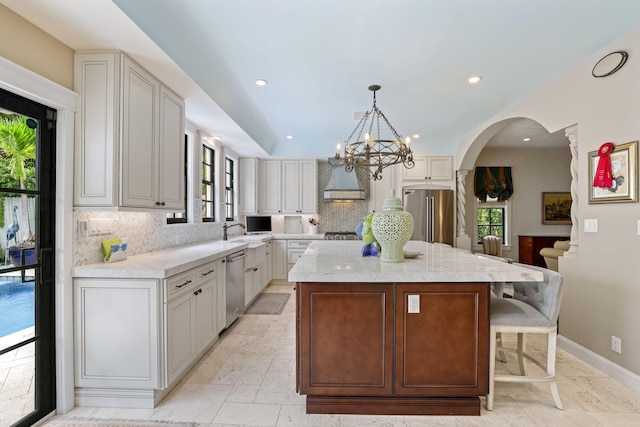 kitchen featuring stainless steel appliances, plenty of natural light, wall chimney range hood, and a center island