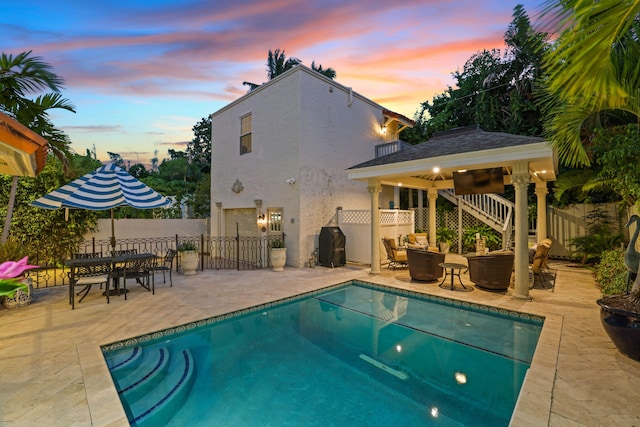 pool at dusk featuring ceiling fan, a patio area, and a gazebo