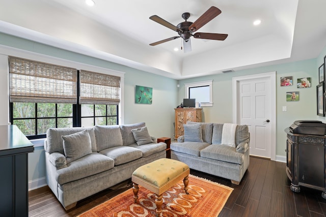 living room with a tray ceiling, dark wood-type flooring, ceiling fan, and a wealth of natural light